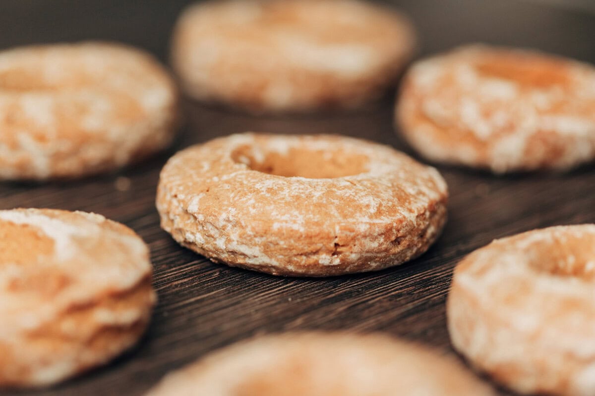Close-up of several round, powdered cookies with holes in the center, arranged on a dark wooden surface.