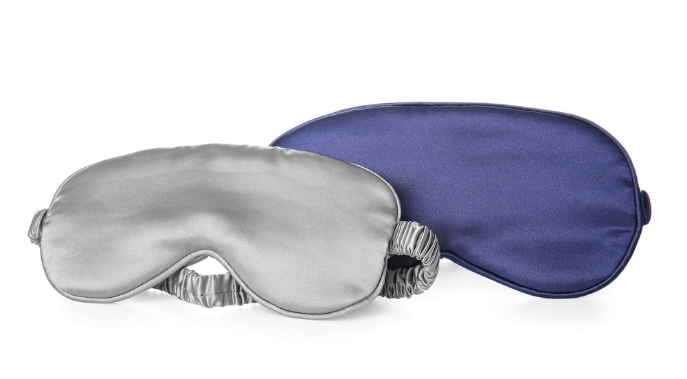 Two sleep masks are shown, one silver and one dark blue, both with elastic straps, placed on a white background.
