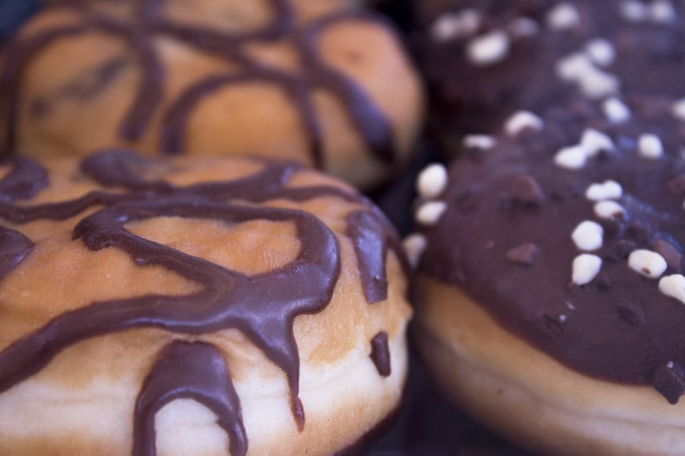 Close-up of four chocolate-covered donuts, two with drizzled chocolate icing and two with chocolate icing topped with white and dark sprinkles.