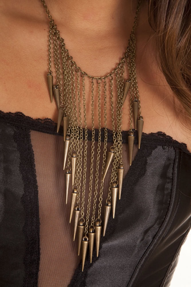 A person wearing a black, strapless, sheer-panel corset and a layered gold chain necklace with multiple cone-shaped pendants.