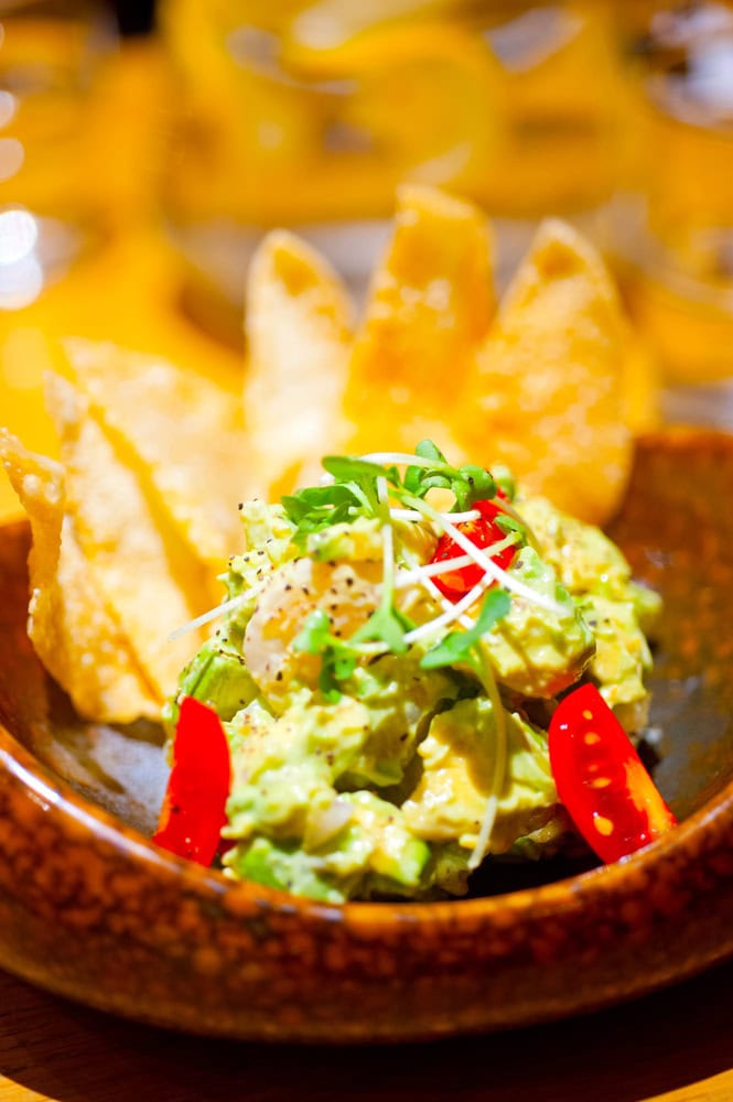 A bowl of guacamole topped with microgreens and sliced cherry tomatoes, served with crispy tortilla chips.