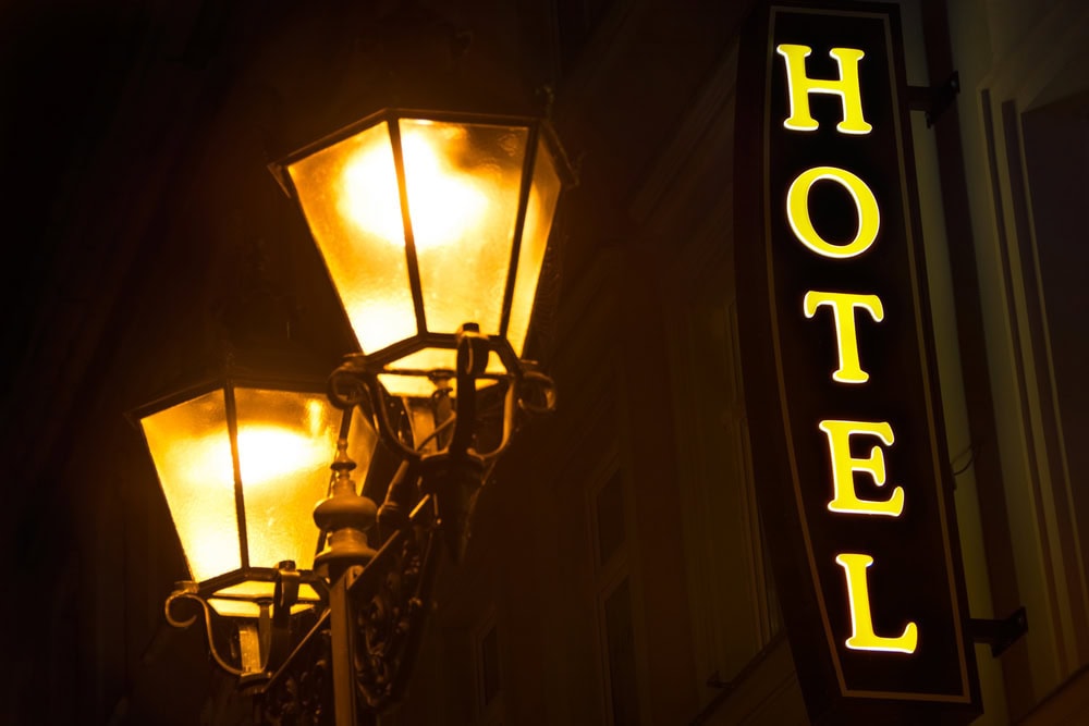 Two illuminated street lamps at night beside a building with a vertical sign that reads "HOTEL" in yellow letters.