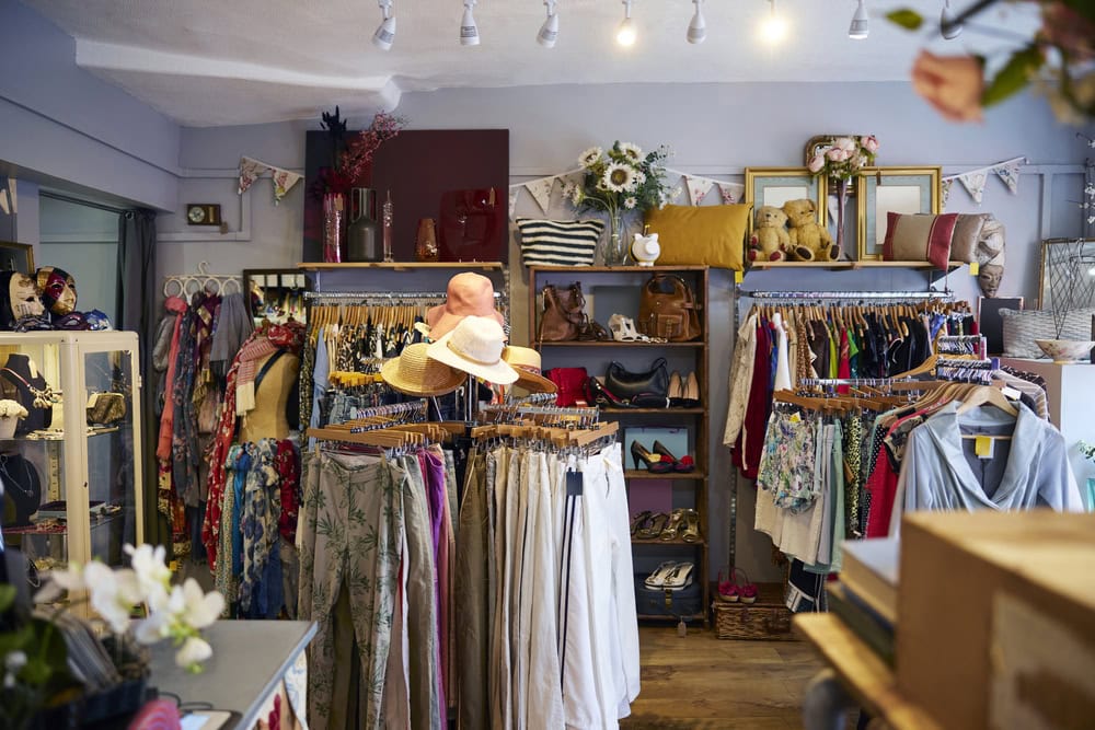 Clothing boutique interior with racks of assorted clothes, hats, bags, and accessories displayed neatly in a well-lit, organized space.