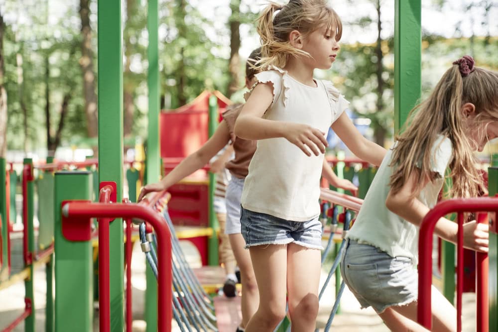 Children playing on colorful playground equipment outdoors, with trees in the background.