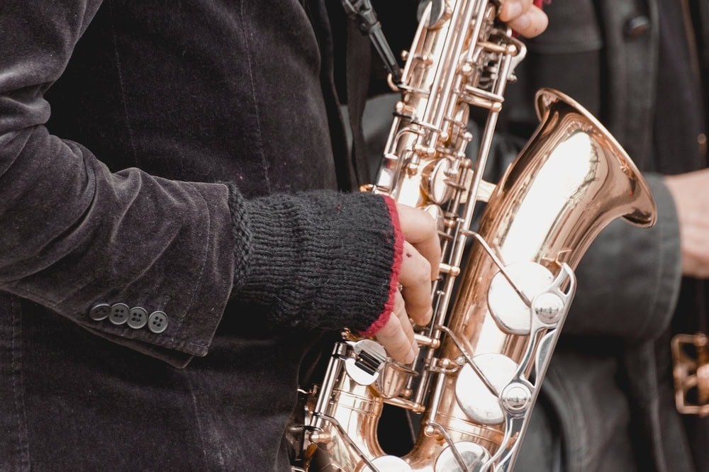 Person wearing a black jacket and fingerless gloves playing a shiny saxophone.