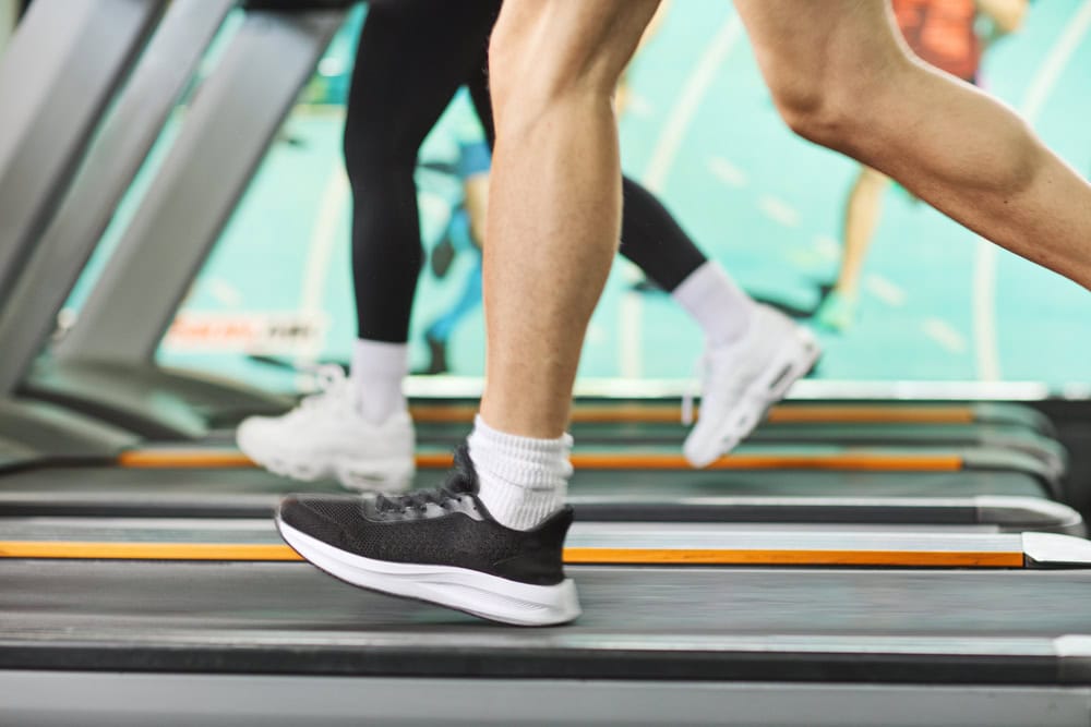 Two people are running on treadmills indoors; only their legs and feet in athletic shoes are visible.