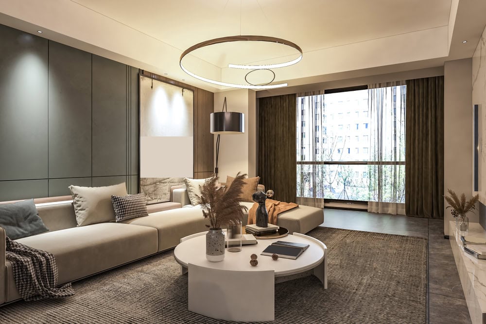 Modern living room with a large sectional sofa, round coffee table with decor, floor lamp, and large windows with sheer curtains letting in natural light.