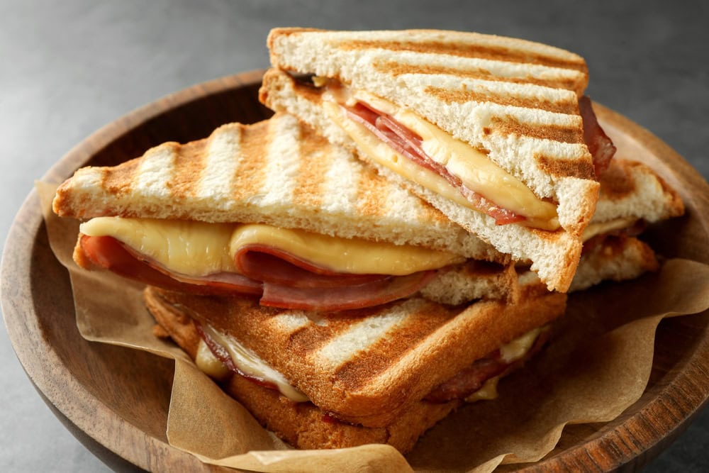 Grilled ham and cheese sandwiches cut in halves, stacked on a wooden plate lined with parchment paper.