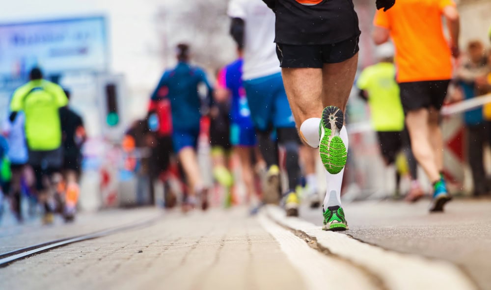 A group of runners participate in a road race, with the focus on the legs and shoes of one runner in the foreground.