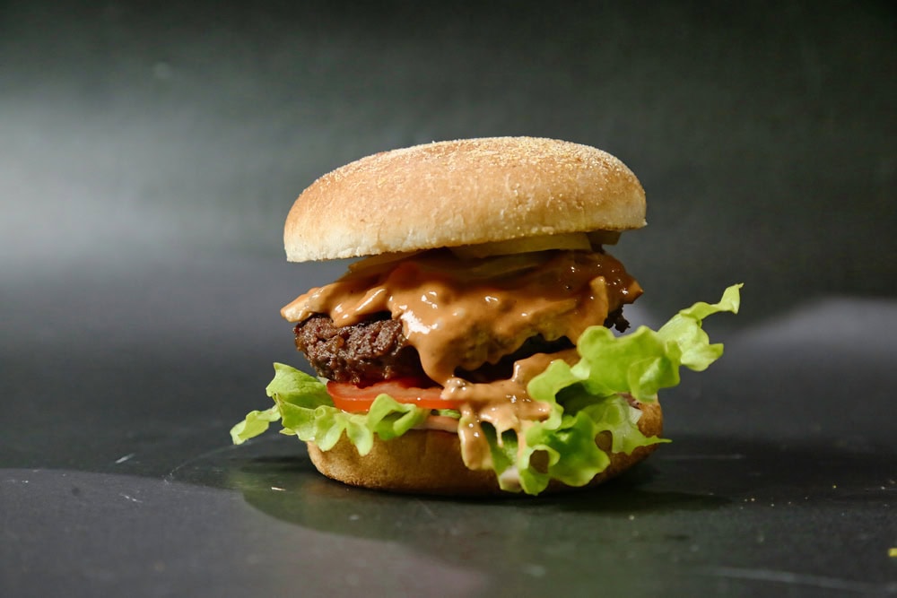 A hamburger with lettuce, tomato, a beef patty, sauce, pickles, and a bun, set against a dark background.