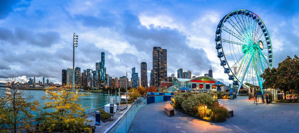 A cityscape view of downtown Chicago with skyscrapers, a waterfront, and a large Ferris wheel lit up at Navy Pier during dusk.