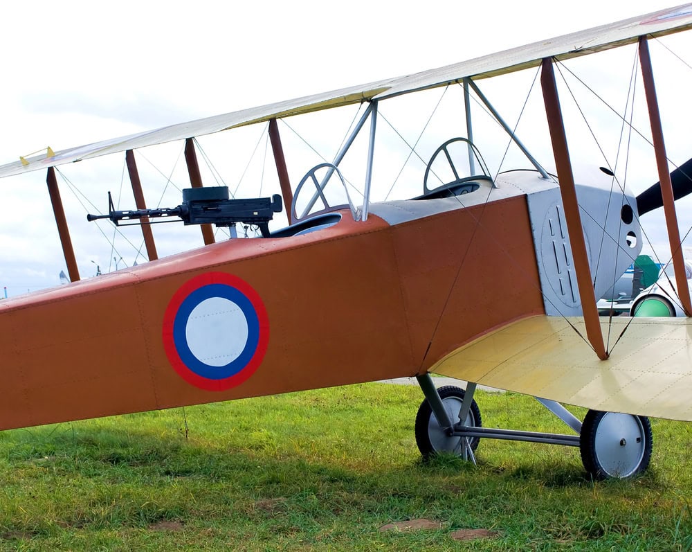 A vintage biplane with a roundel insignia and a mounted machine gun is parked on grass.