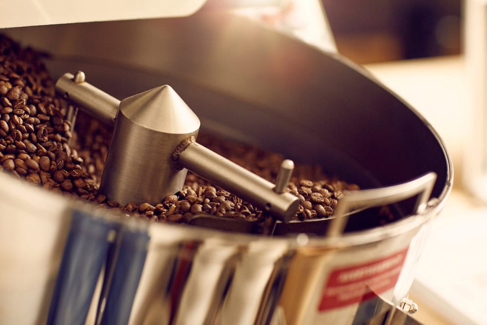 Close-up of coffee beans being roasted in a commercial coffee roasting machine with a metal agitator.