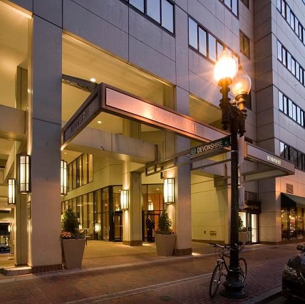A modern building entrance with large pillars, illuminated street lamps, and a bicycle parked on the sidewalk near a street sign reading 