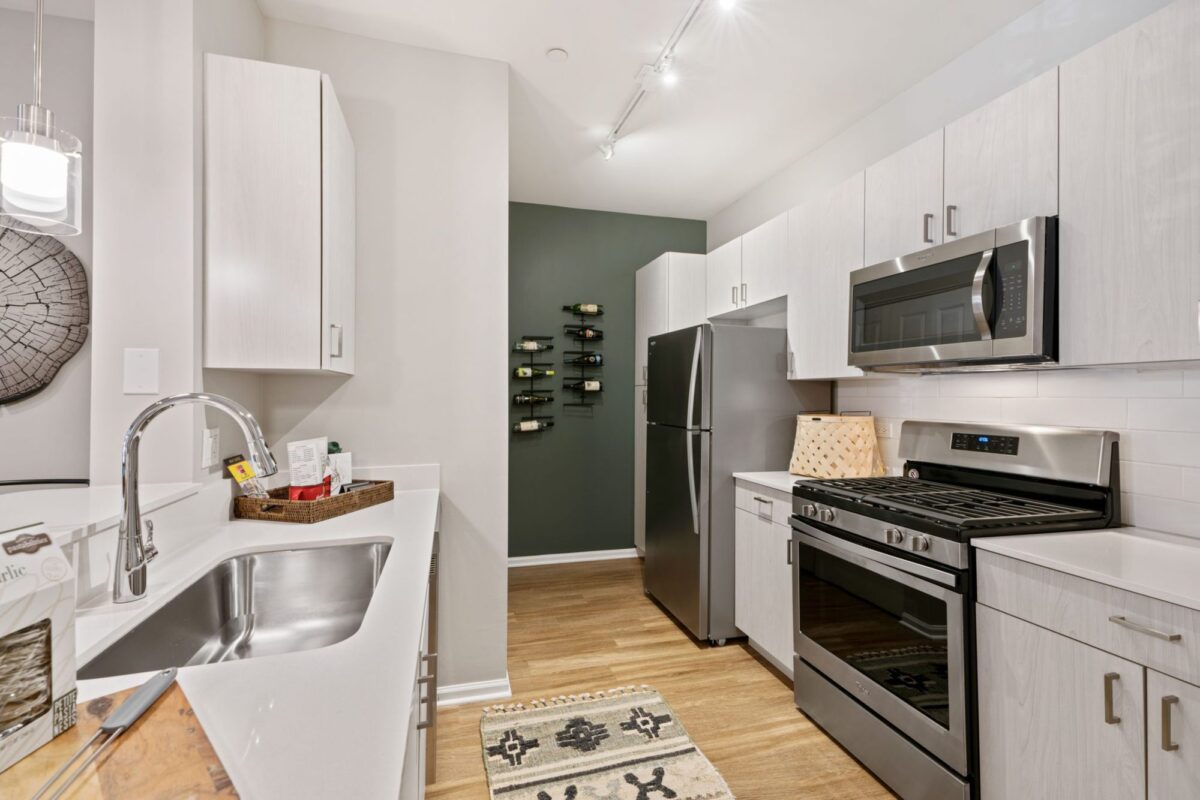 Modern kitchen with stainless steel appliances, white cabinets, a double sink, wall-mounted wine rack, and wood flooring.