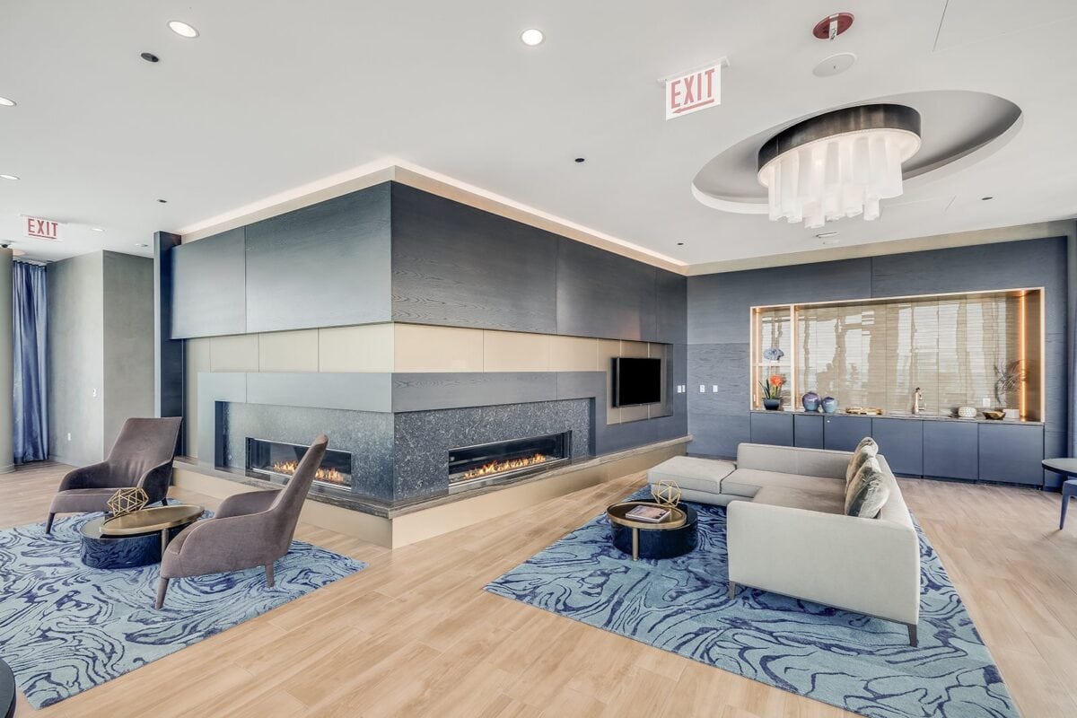 Modern lounge with a long gas fireplace, contemporary chairs and sofas, blue accent rugs, and decorative shelving against a light wood floor.