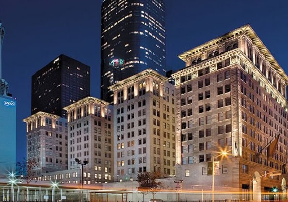 Historic multi-story buildings with illuminated architectural details stand in front of modern glass skyscrapers at dusk in an urban downtown setting.