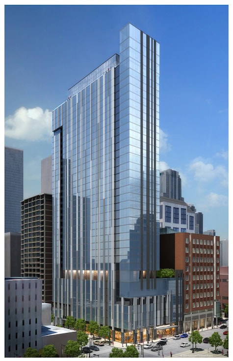 Tall, modern glass skyscraper with reflective windows, surrounded by shorter buildings on a city street under a blue sky.