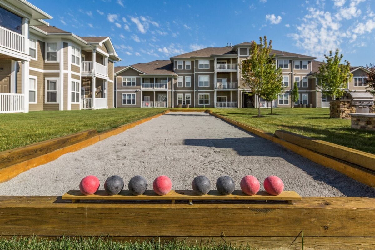 A bocce ball court with four red balls and four black balls lined up on a wooden plank, with apartment buildings in the background.