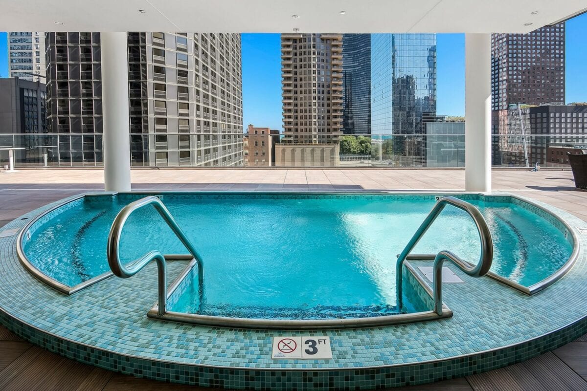 Circular swimming pool with tiled edge on an outdoor deck, surrounded by city skyscrapers; metal handrails and a 3-foot depth marker are visible.