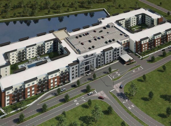 Aerial view of a large modern apartment complex with a central parking area, surrounding green spaces, and a nearby pond.