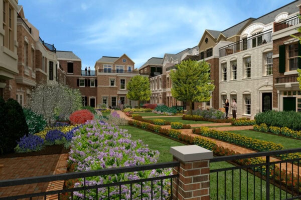 A landscaped courtyard with gardens, green lawns, and flower beds, surrounded by multi-story brick townhouses under a clear blue sky.