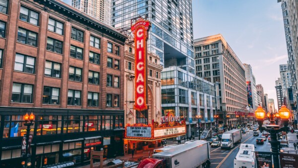 Street view of downtown Chicago featuring the iconic Chicago Theatre sign, surrounded by buildings, traffic, and pedestrians under a clear sky.