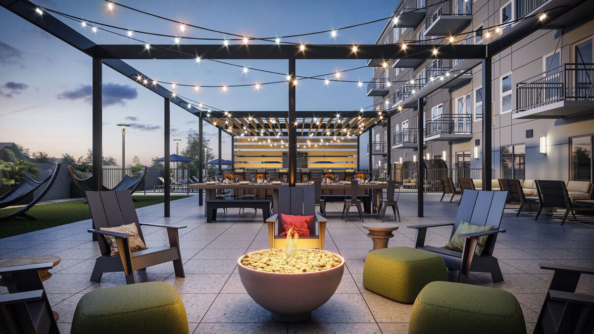 Outdoor patio with string lights, fire pit surrounded by chairs and ottomans, dining tables in the background, and modern apartment balconies overlooking the space at dusk.